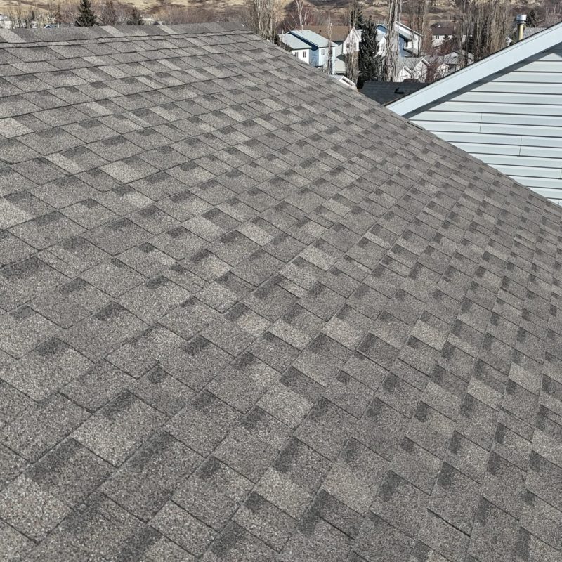 Drone flying over Calgary home casting shadow on shingle roof.